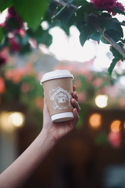 Kape Maria takeaway cup held up among flowers